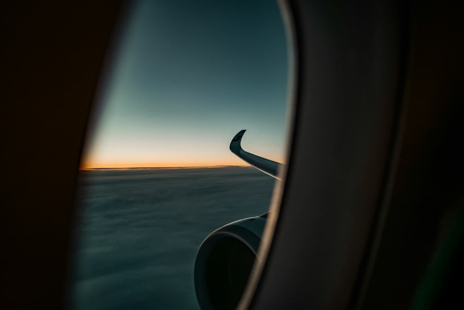 Airplane wing seen through a cabin window at sunset above the clouds