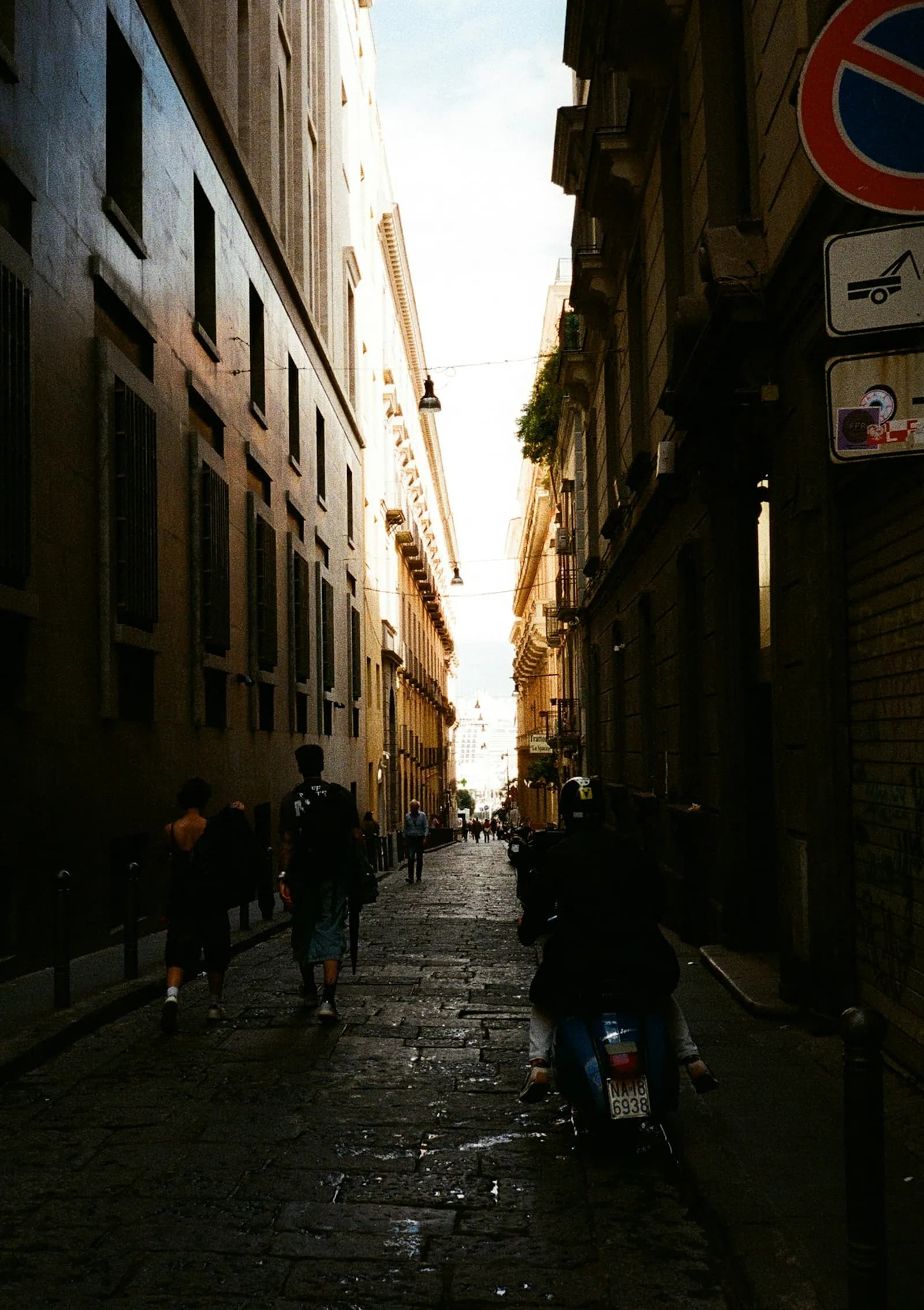 A narrow sunlit street with a scooter in Naples