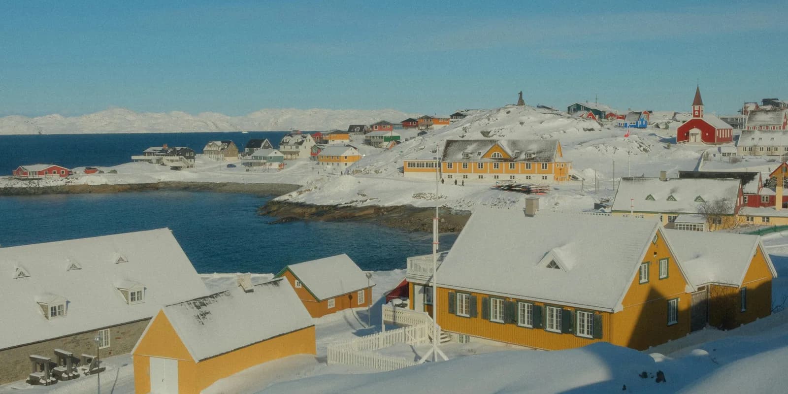 Colourful Nuuk houses beside a snowy harbour and mountains