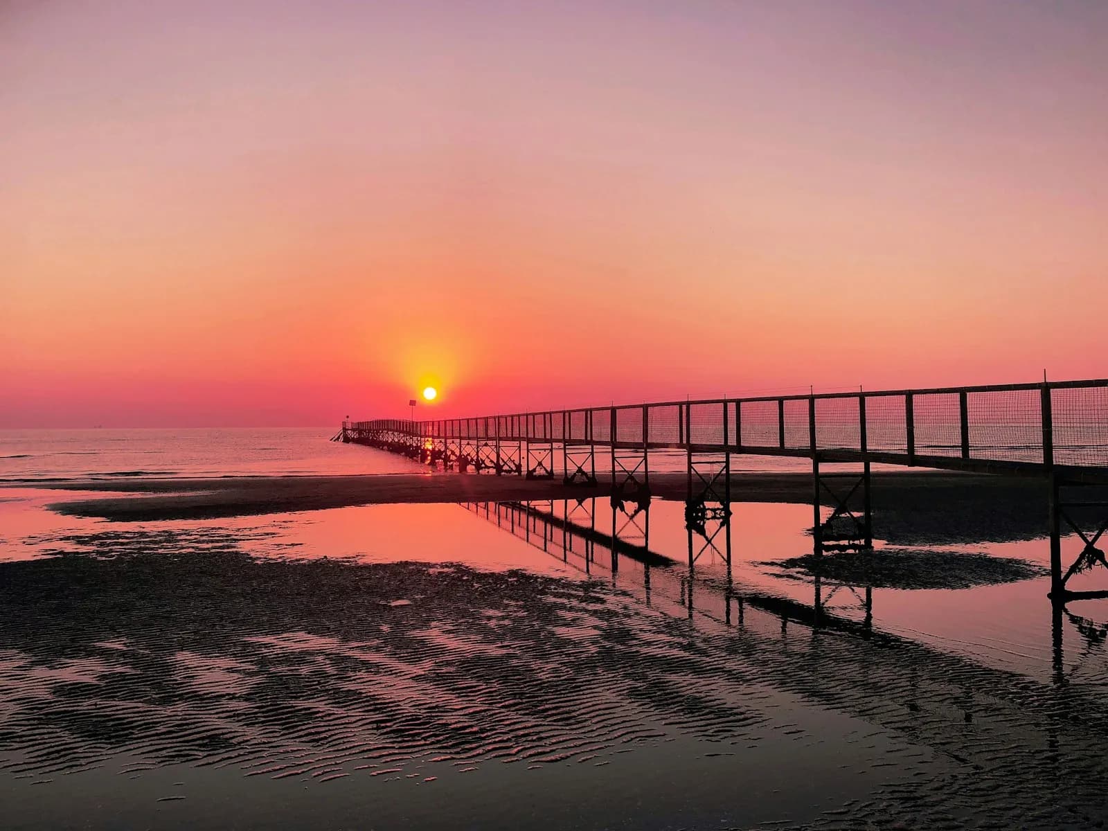 A pier silhouetted at sunset on Rimini's Adriatic beach