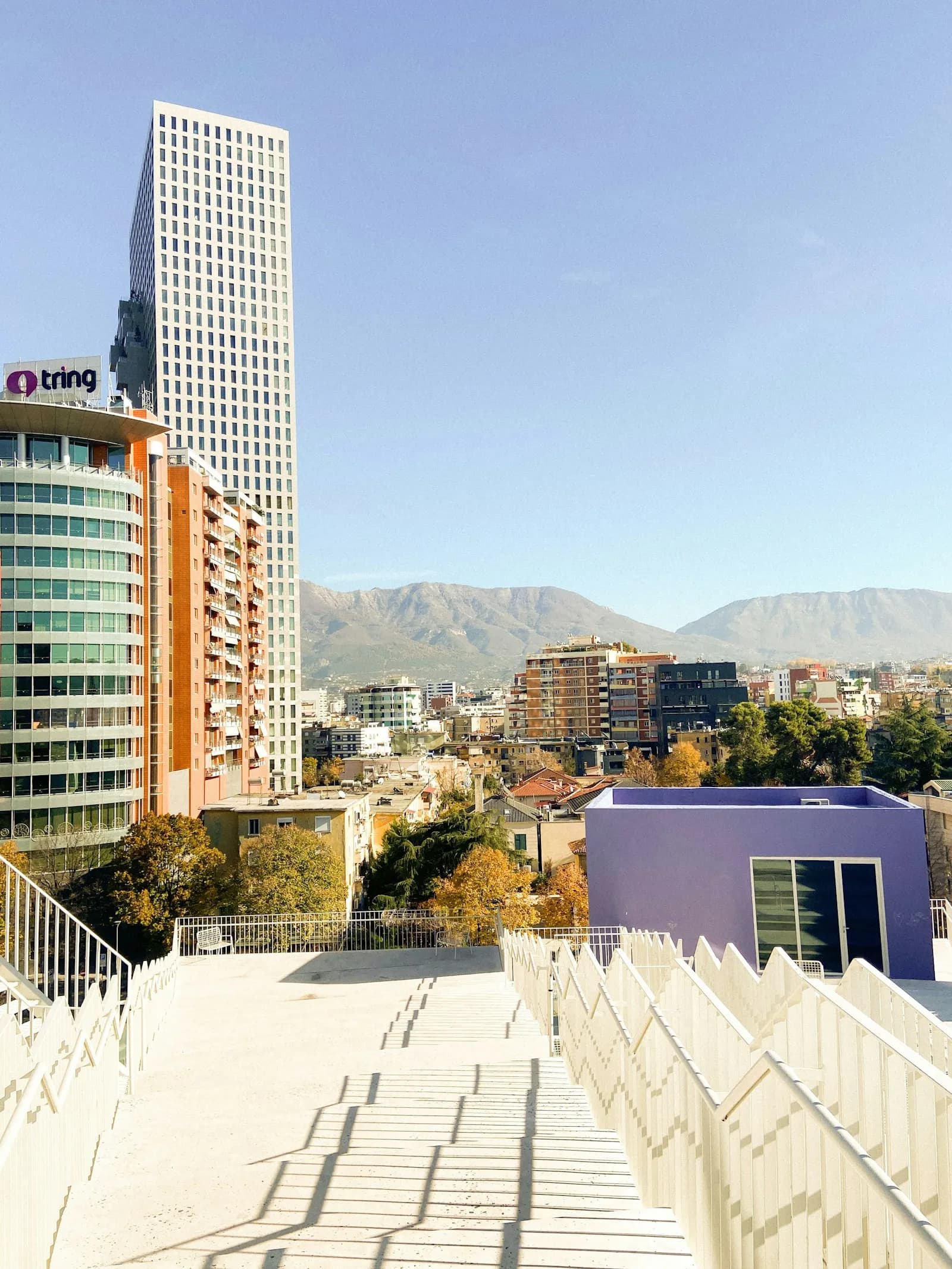 Modern towers and mountain backdrop from a white walkway in Tirana